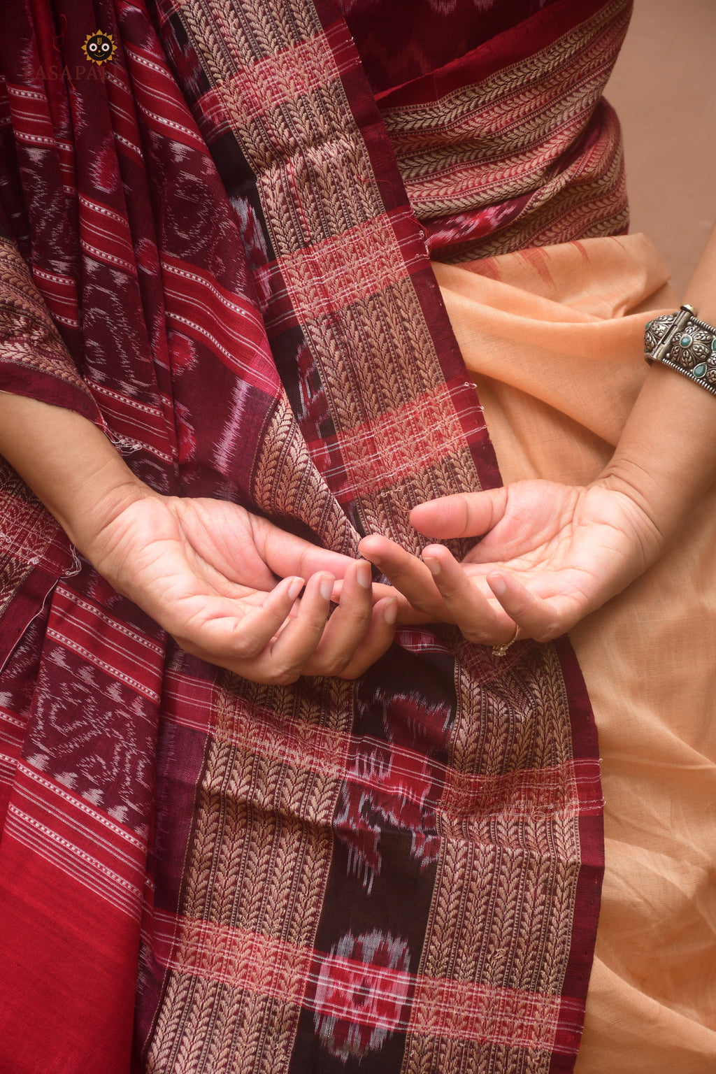 Sunanda Sambalpuri Bandha saree flat lay — light brown mercerized cotton with maroon pallu and chevron border detail