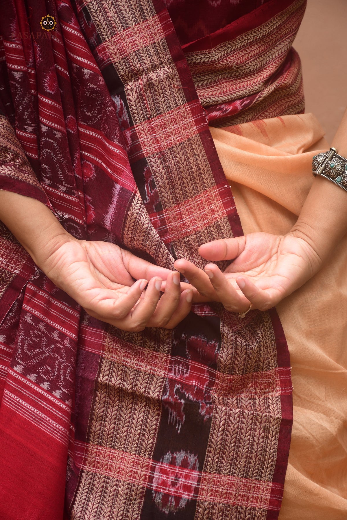 Sunanda Sambalpuri Bandha saree flat lay — light brown mercerized cotton with maroon pallu and chevron border detail